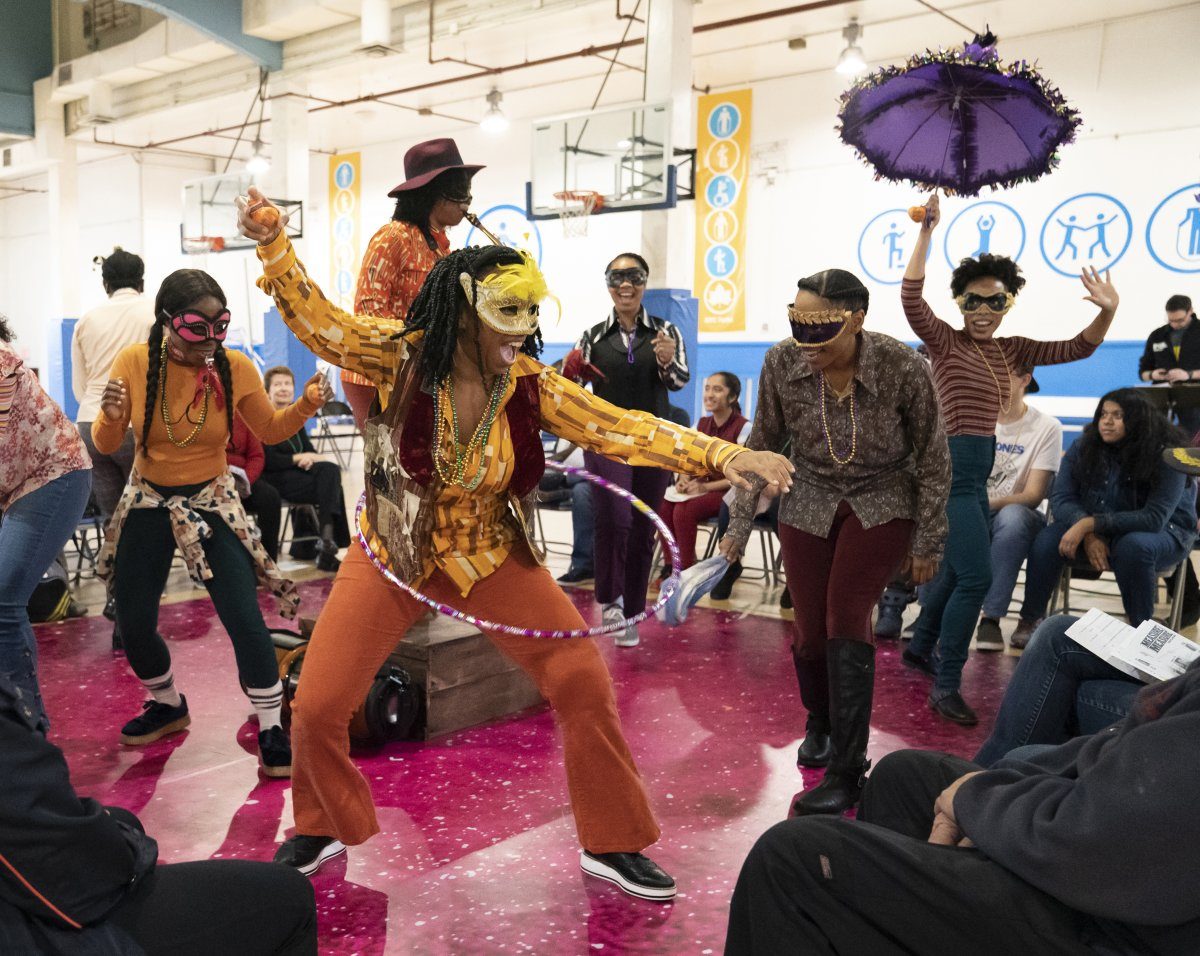 The cast of "Measure for Measure," dressed in Mardi Gras clothing, performs in a gymnasium