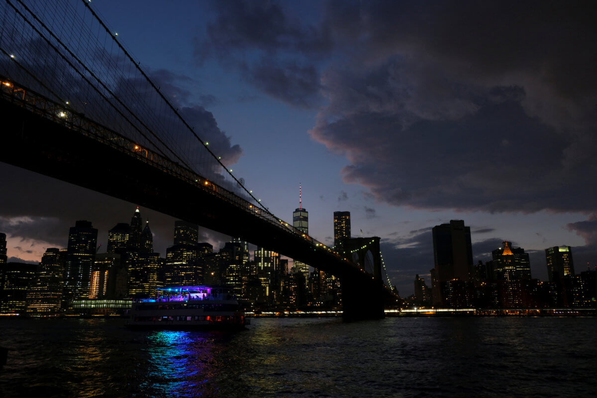 A ferry boat passes under Brooklyn Bridge in front of the night skyline of Lower Manhattan in New York City