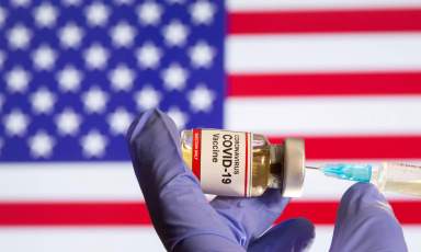 FILE PHOTO: A small bottle labeled with a “Coronavirus COVID-19 Vaccine” sticker and a medical syringe in front of displayed USA flag in this illustration