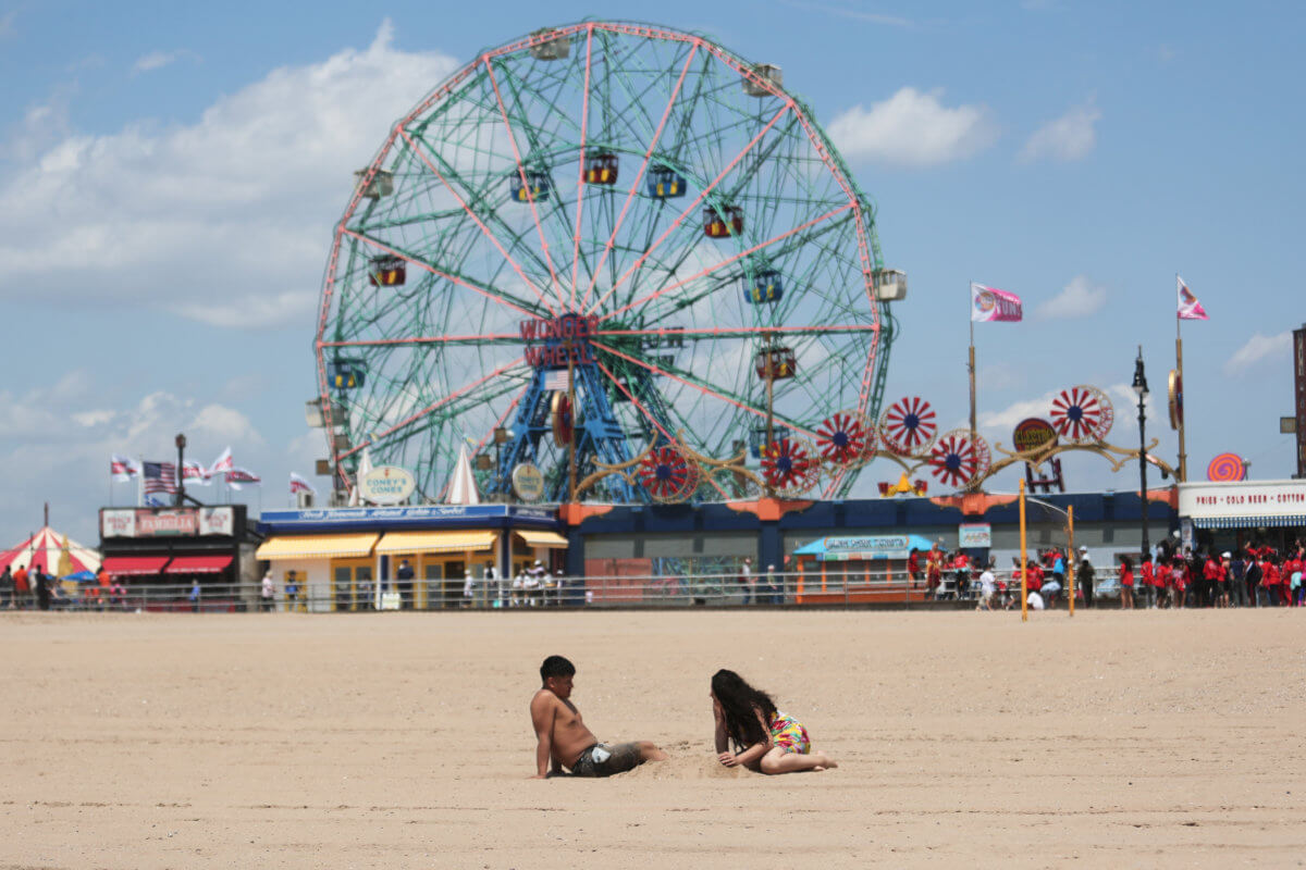People sit on the sand during warm weather at Coney Island in the Brooklyn borough of New York