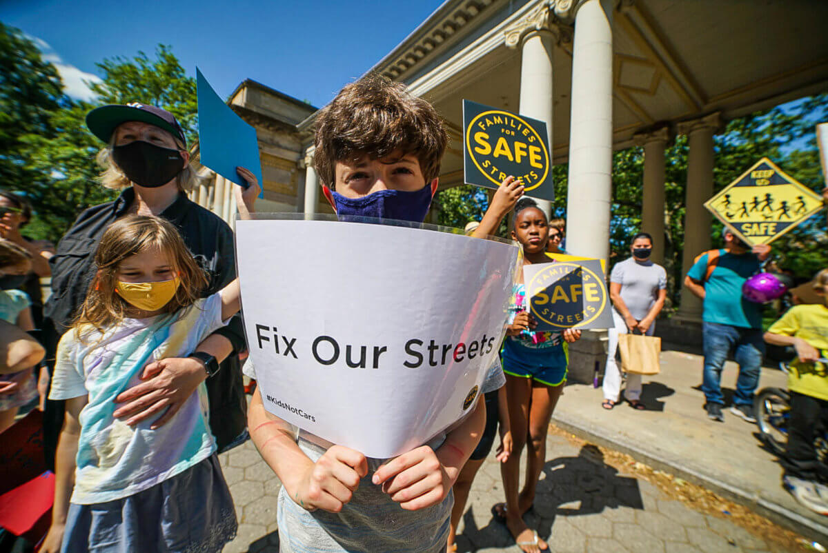 child holding sign that says "fix our streets" at mcguinness boulevard