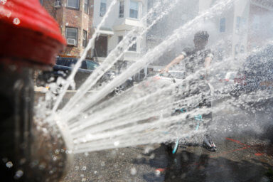 A boy on a bicycle cools off from the extreme heat from an opened fire hydrant in Brooklyn, New York