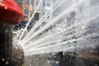 A boy on a bicycle cools off from the extreme heat from an opened fire hydrant in Brooklyn, New York