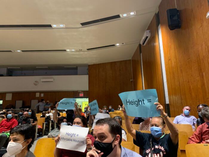 People hold signs at a community board meeting