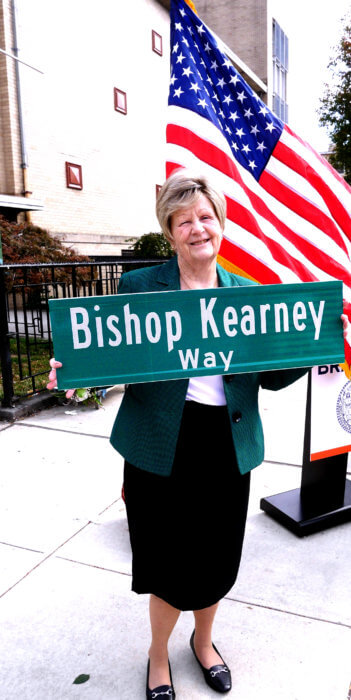 helen kearney with a street sign that says bishop kearney way