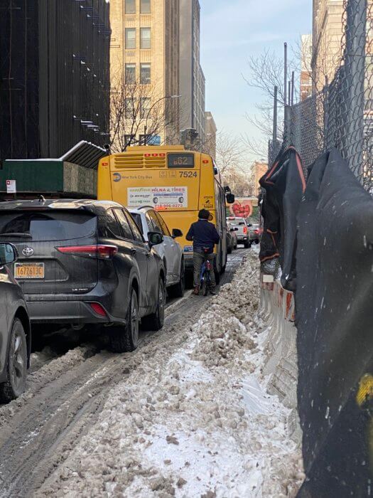 lincoln restler rides his bike over snow and next to parked cars and buses during the schermerhorn challenge