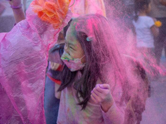 girl in a mask covered in pink powder at a holi festival