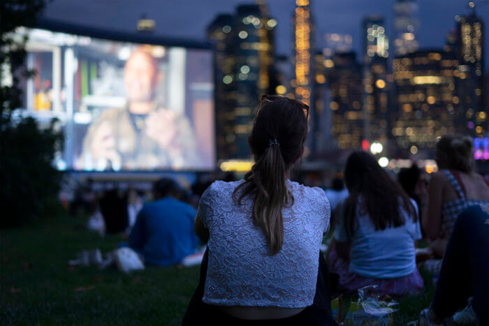 woman sitting on lawn watching movie with nyc skyline behind at movies with a view