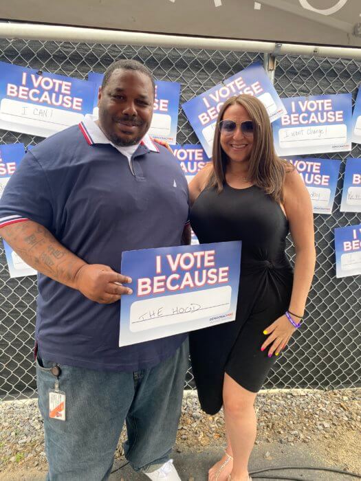 district leader dana rachlin, woman in black dress, stands with a man holding a sign that says "I vote because"