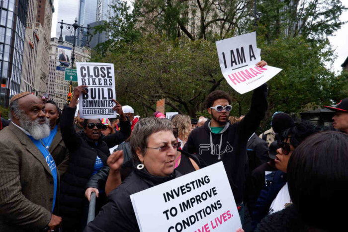 people hold signs at rally to close rikers island