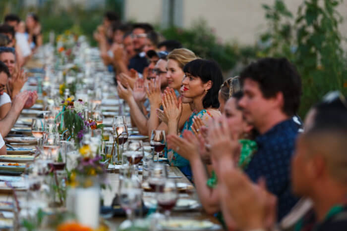 a row of people sitting on one side of a table clap