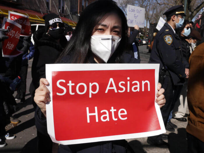 woman holding sign at anti-asian hate rally asian community watch group