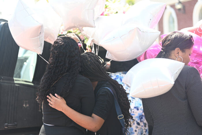 two women hug behind hearse after funeral