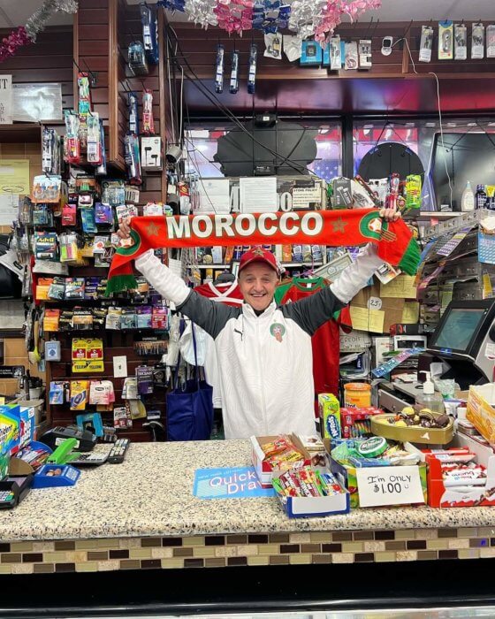 deli owner holds up morocco scarf for world cup