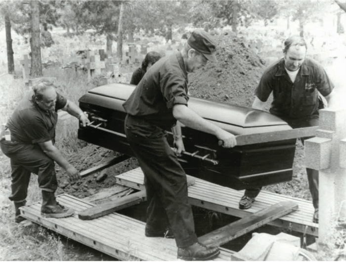 priest lowers coffin into ground during gravedigger's strike
