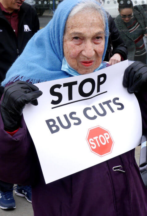 A protestor with a blue headscarf holds a sign at an MTA bus protest in southern Brooklyn.
