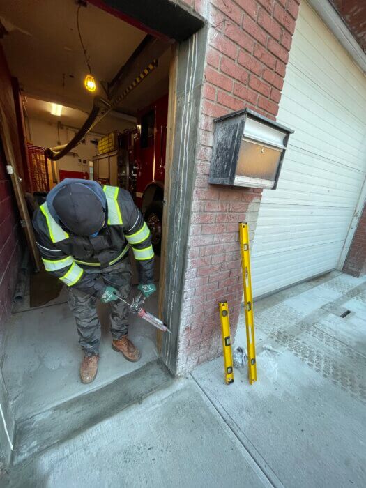 Photo of a man in a construction uniform applying sealant to the door of the Gerritsen Beach Fire Department.