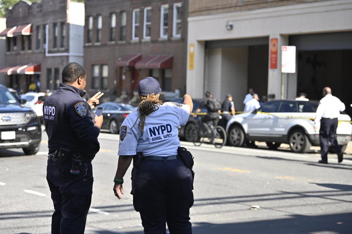 Police officers gesture towards the scene of a triple stabbing outside of Brownsville Academy High School.