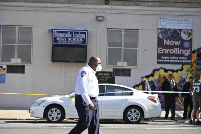Police officers walks by the scene of a triple stabbing outside of Brownsville Academy High School.