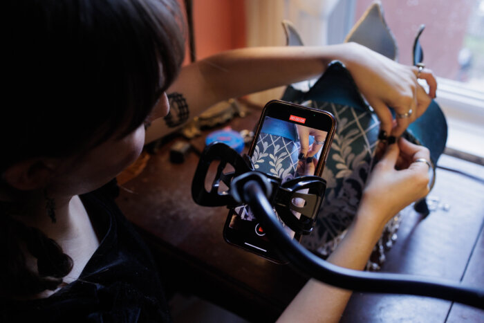 Ivy Karlsgodt works on a lamp shade and films it for social media in her Bedford-Stuyvesant home studio on Tuesday, March 5, 2024. Karlsgodt hand makes the shades for her business, Ace of Shades.