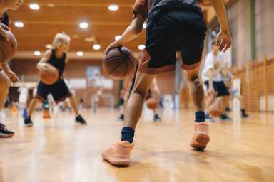 Junior level basketball player bouncing basketball. Young basketball player with classic ball. Basketball training session for youth. School sports class