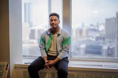council member chi ossé sitting on the window sill in his office in a green and blue jacket