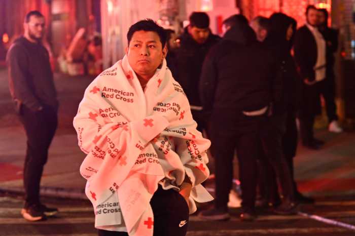 A displaced resident wrapped in an American Red Cross blanket stands outside 3901 13th Ave. in Borough Park