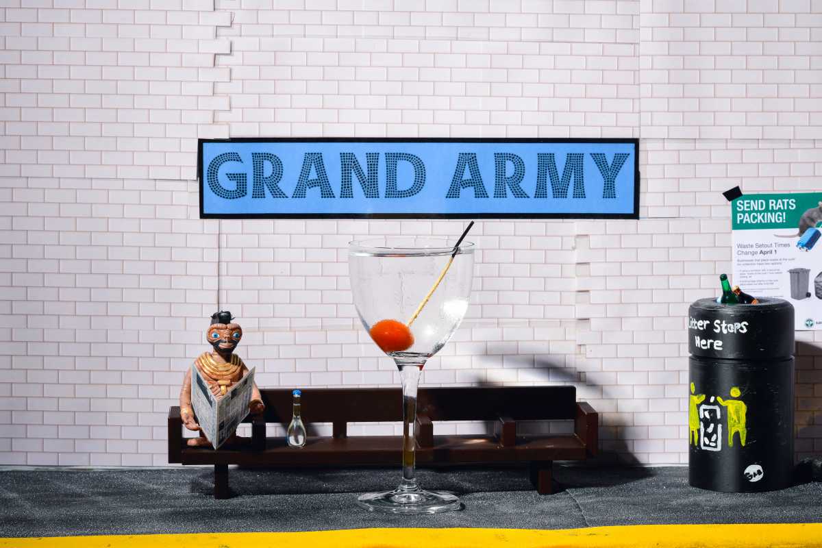 tiny MTA diorama with subway bench and cocktail in front of grand army plaza sign at grand army bar