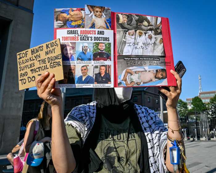 protester outside brooklyn navy yard holding signs showing gazan children